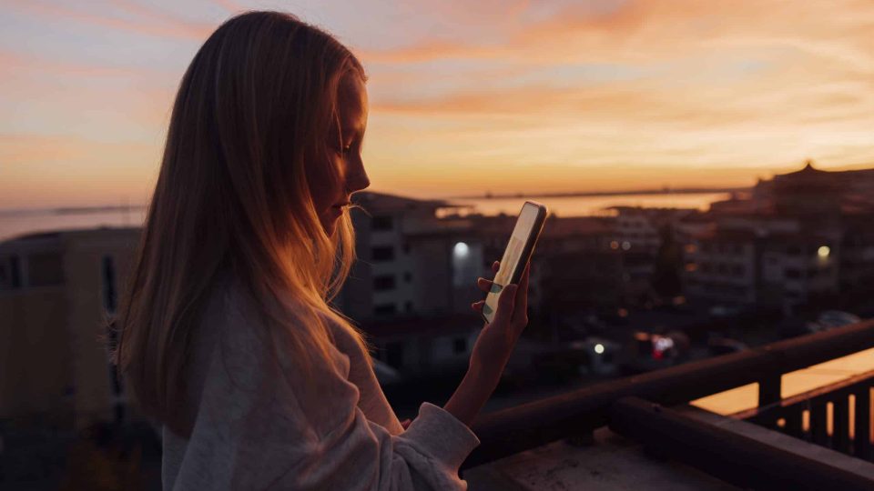 Girl enjoying sunset on rooftop capturing moment with smartphone in warm evening light, Bulgaria, Sveti Vlas