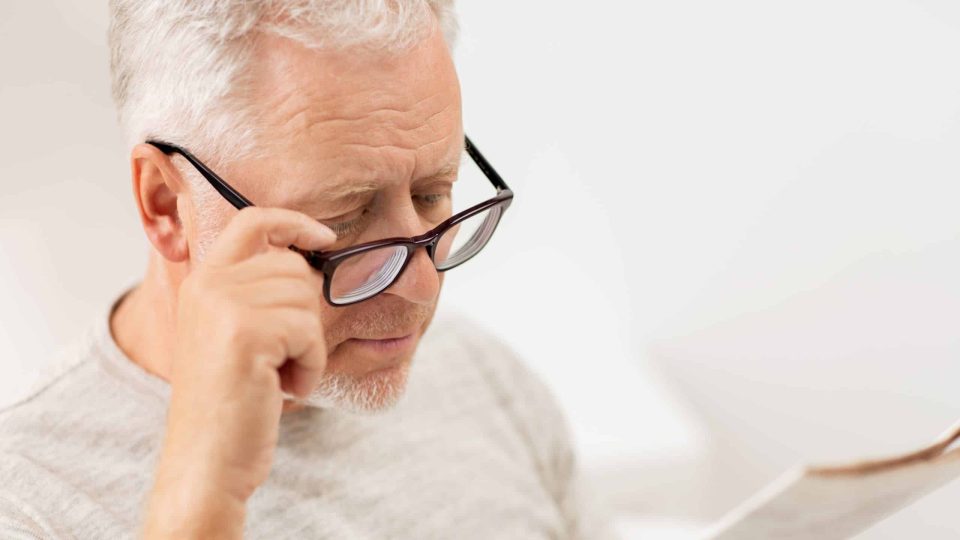 leisure, information, people, vision and mass media concept - close up of senior man in glasses reading newspaper at home