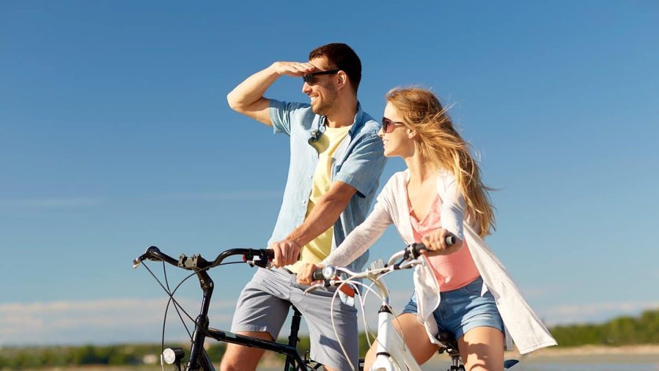 people, leisure and lifestyle concept - happy young couple riding bicycles on beach