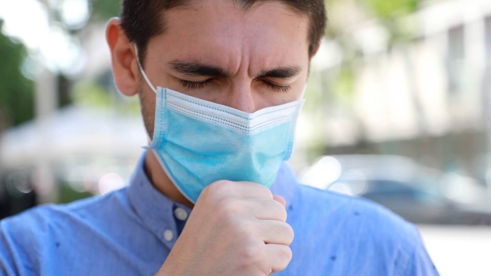 COVID-19 Close Up Sick Man Wearing Surgical Mask Coughing in City Street. Portrait of Man with Face Mask Against SARS-CoV-2 Coughing Outdoor.